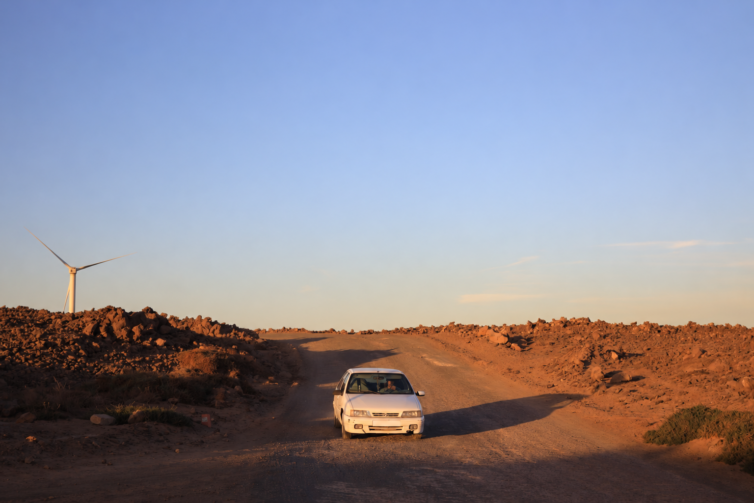 A white car on a volcanic road at golden hour