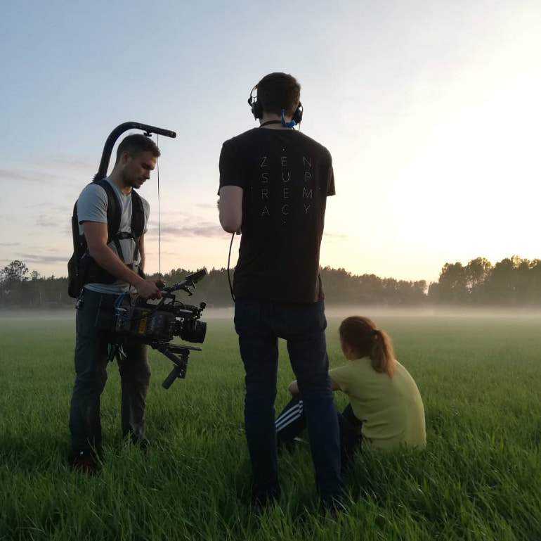 Cameraman filming an actor on a field of grass.